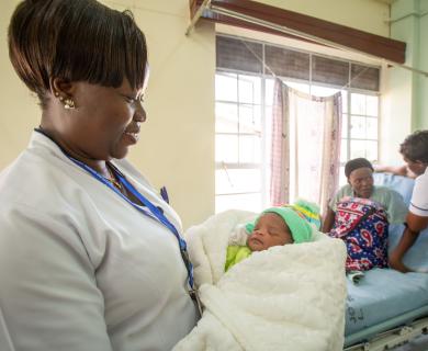 A midwife holds a swaddled newborn.