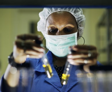 Black woman in mask holds up test tubes