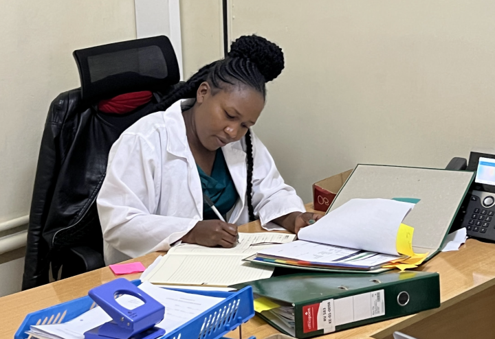 A woman in a lab coat writes in a binder at a desk