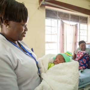 A midwife holds a swaddled newborn.